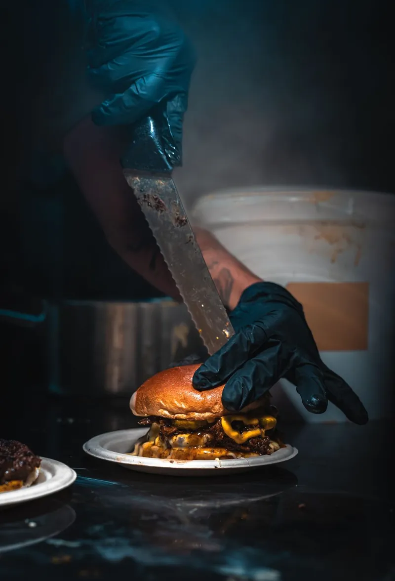 Grillmaster składa burgera nożem przy stanowisku